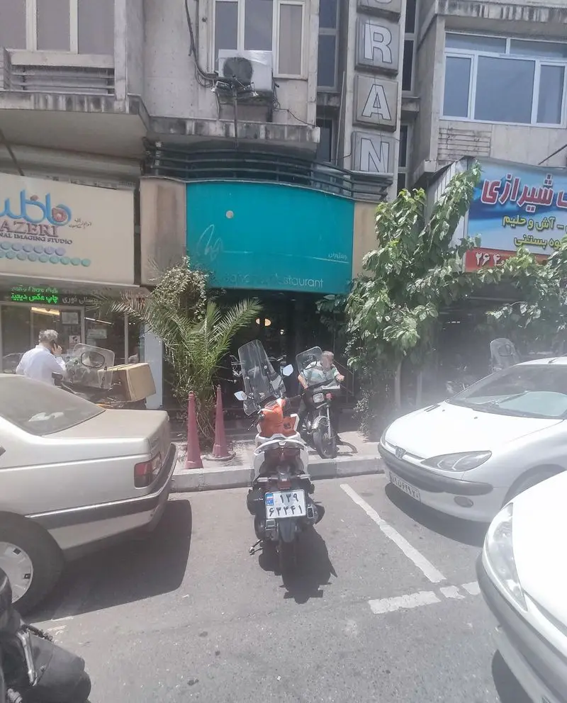 نمای بیرونی رستوران سهند در روز، با تابلوی آبی رنگ و خودروهای پارک شده در خیابان، نشان‌دهنده فعالیت شهری در تهران.