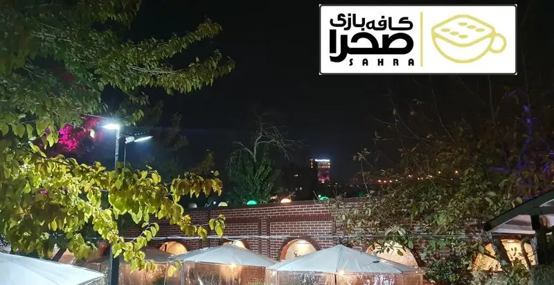 فضای باز دلنشین کافه بازی صحرا در شب با نورپردازی، درختان، دیوارهای آجری و مکان‌های خصوصی، ایده‌آل برای سرگرمی و جمع‌های دوستانه.