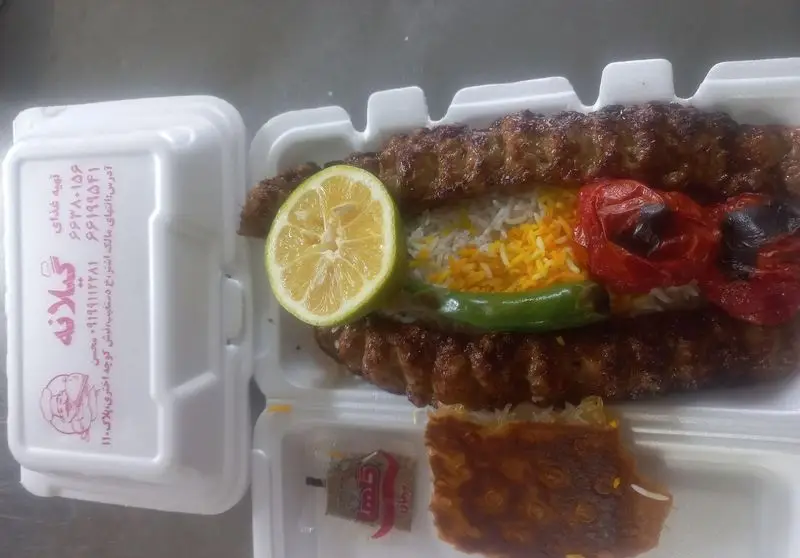 تصویری از یک پرس کباب کوبیده لذیذ از تهیه و توزیع غذای گیلانه شامل برنج زعفرانی، لیمو، گوجه و ته دیگ در بسته‌بندی.