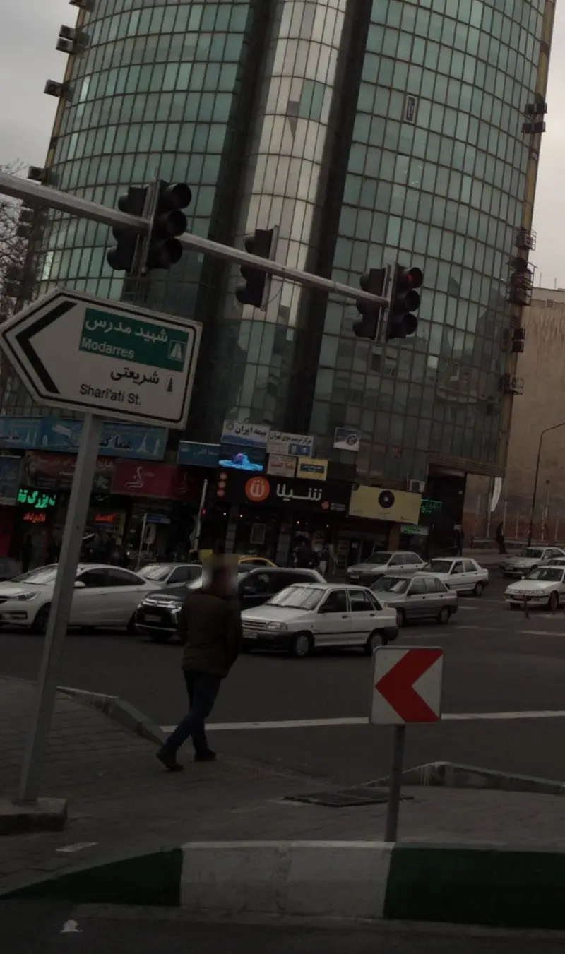 تصویری از تقاطع خیابان شریعتی و مدرس در تهران، همراه با ساختمان‌های اداری، ترافیک شهری و تابلوی فست فود شیلا.