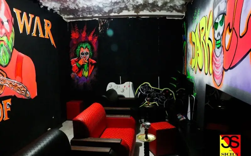 فضای داخلی گیم نت شبانه روزی سیسیلی ستارخان با مبلمان قرمز، دیوارنگاری جذاب جوکر و قلیان، محیطی مهیج برای گیمرها.