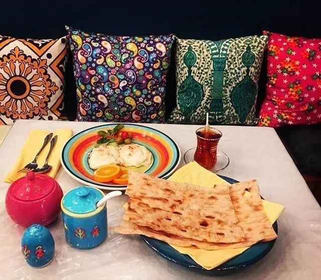 صبحانه سنتی ایرانی در رستوران دیزی شاپ؛ میز رنگارنگ با تخم مرغ، نان داغ، چای و بالشتک‌های زیبا، فضایی دلنشین.