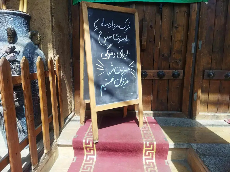 ورودی کافه شمعدونی با تابلو اعلانات منوی متنوع و فصلی جدید. فرش قرمز و دکور چوبی سنتی کافه.