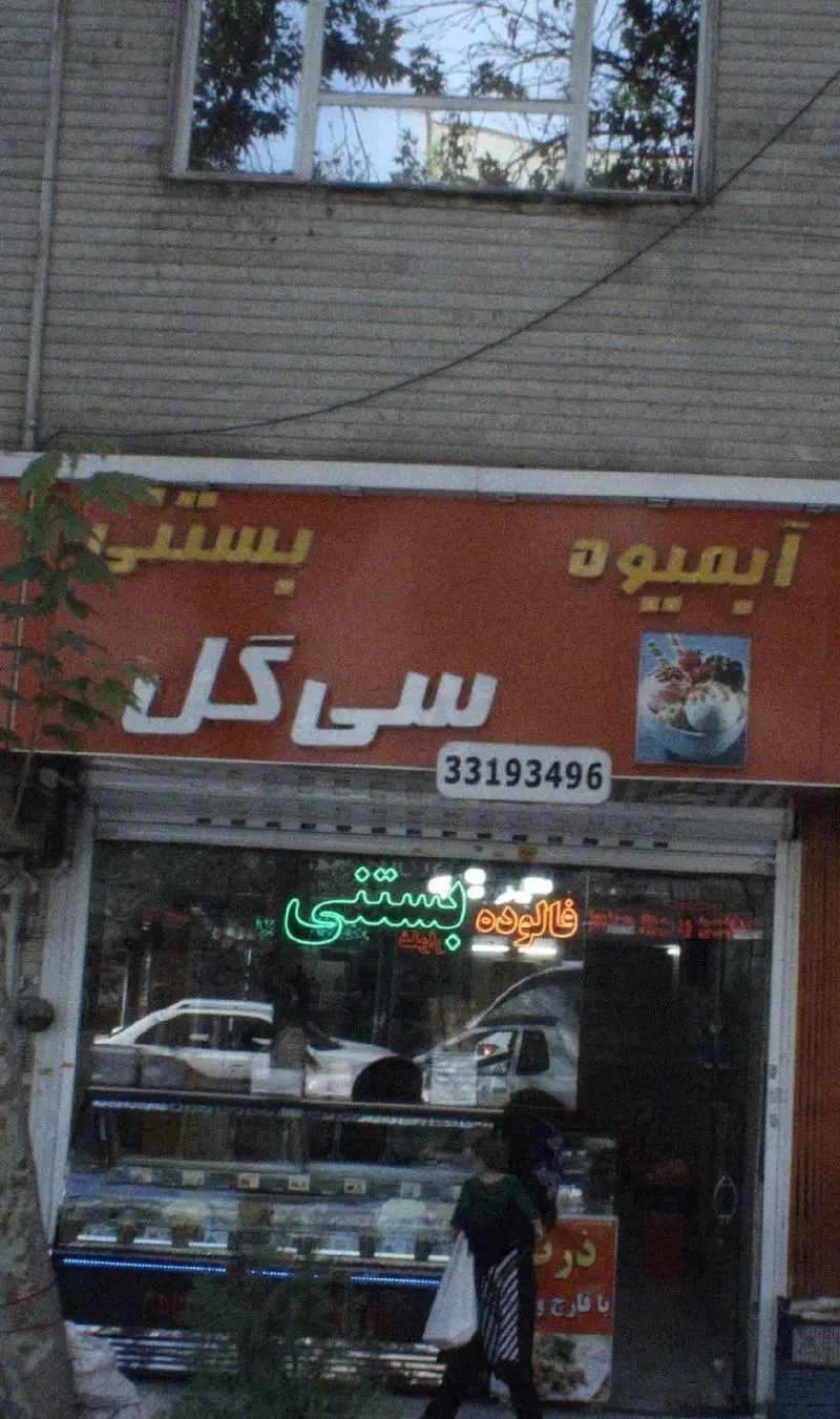 نمایی از مغازه آبمیوه و بستنی سی گل با تابلوی قرمز رنگ، شماره تلفن و ویترین محصولات مختلف از جمله بستنی و فالوده.