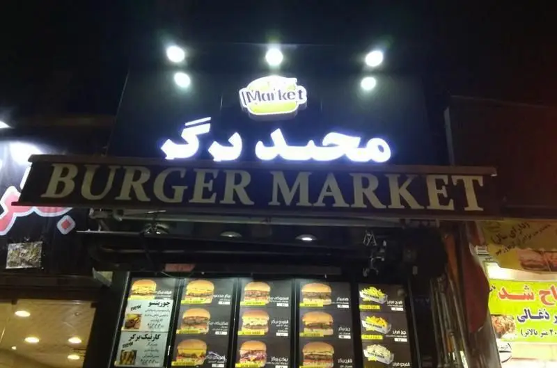نمای بیرونی جذاب فست فود "مجید برگر" (Burger Market) در شب، با تابلوهای نئونی درخشان و منوی متنوع شامل انواع همبرگر و سیب‌زمینی.