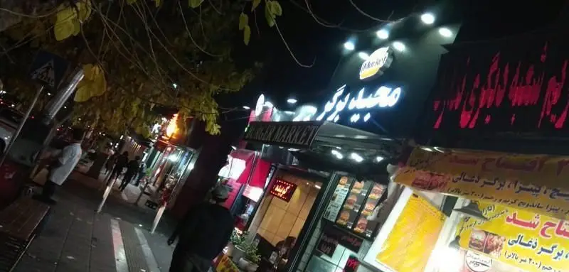 تصویری شبانه از نمای بیرونی فست فود مجید برگر با تابلوی نئون روشن، ارائه دهنده انواع برگر و ساندویچ در محیطی پرجنب‌وجوش شهری.