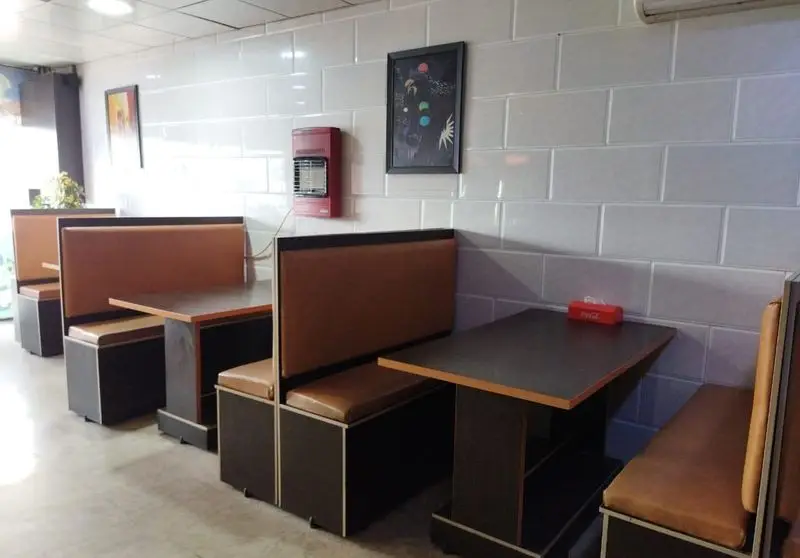 فضای داخلی فست فود ماموت با میز و صندلی‌های چوبی و قهوه‌ای، دیوارهای کاشی‌کاری شده سفید و دکوری ساده و تمیز برای مشتریان.