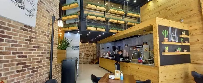 فضای داخلی شیک و مدرن فست فود برگراتور با طراحی آجری و چوبی، پیشخوان سفارشات و گیاهان آویز زیبا برای مشتریان.