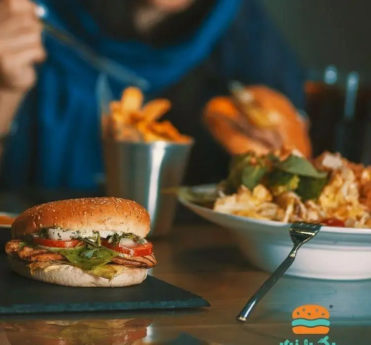 برگراتور: برگر مرغ گریل شده تازه با گوجه و کاهو، همراه سیب زمینی سرخ کرده در فضای دنج رستوران فست فود برگراتور.
