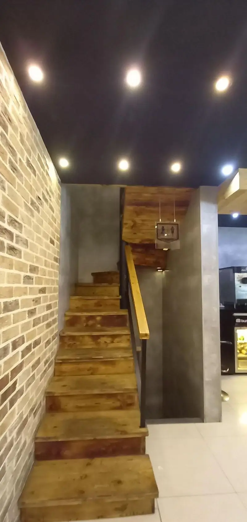 تصویری از فضای داخلی فست فود برگراتور: پله‌های چوبی، دیوار آجری طرح‌دار، سقف با نورهای توکار. دکوراسیون مدرن و جذاب رستوران.