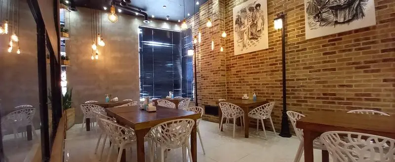 دکوراسیون مدرن و جذاب فست فود برگراتور با میز و صندلی‌های سفید، دیوارهای آجری و نورپردازی گرم برای تجربه‌ای دلپذیر.