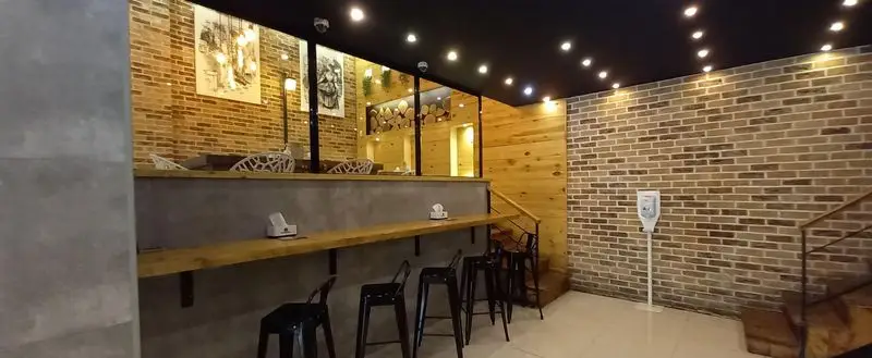 نمایی از فضای داخلی فست فود برگراتور با دکوراسیون شیک و مدرن، دیوارهای آجری و چوبی، سقف نورپردازی شده و میز بار با صندلی‌های بلند.