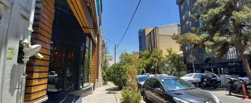 نمای بیرونی فست فود برگراتور با نمای چوبی و شیشه‌ای در خیابان تهران، همراه با خودروها و درختان در یک روز آفتابی.