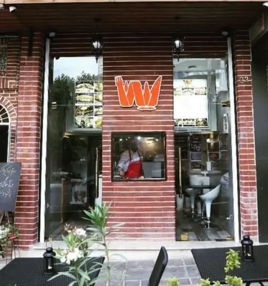 ورودی دلنشین خانه کباب لیانا، رستوران کباب با نمای آجری، لوگوی برجسته، آشپز فعال و میز و صندلی‌های شیک در فضای باز.