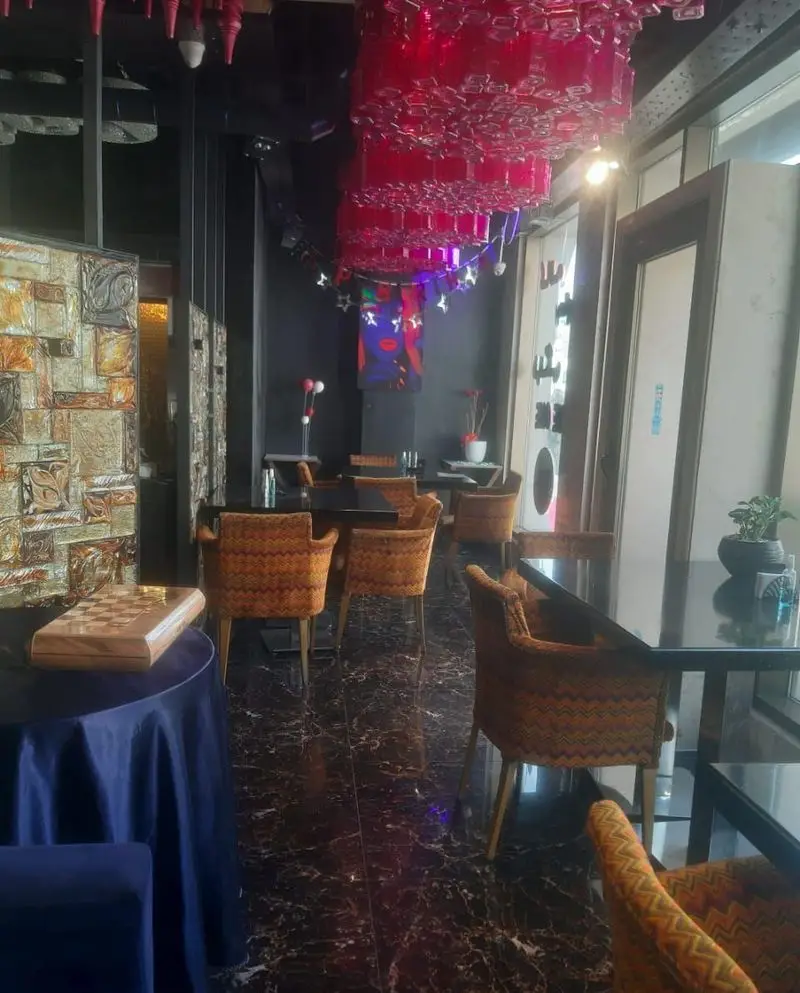 فضای داخلی دلنشین و مدرن رستوران تهران پاریس، با لوستر قرمز منحصر به فرد، صندلی‌های طرح‌دار و میز شطرنج زیبا.