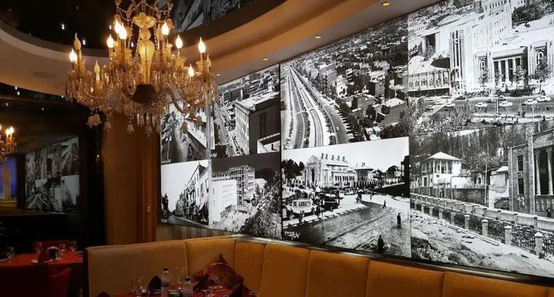 دکوراسیون داخلی رستوران تهران پاریس با لوستر طلایی مجلل و دیوار بزرگ پوشیده از تصاویر تاریخی سیاه و سفید تهران.