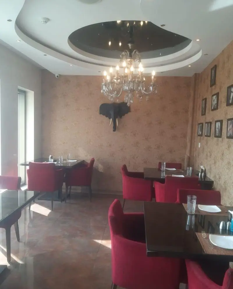 دکوراسیون داخلی لوکس و مدرن رستوران تهران پاریس. شامل صندلی‌های قرمز راحتی، میزهای شیک، لوستر بزرگ و دیوار با طرح خاص.