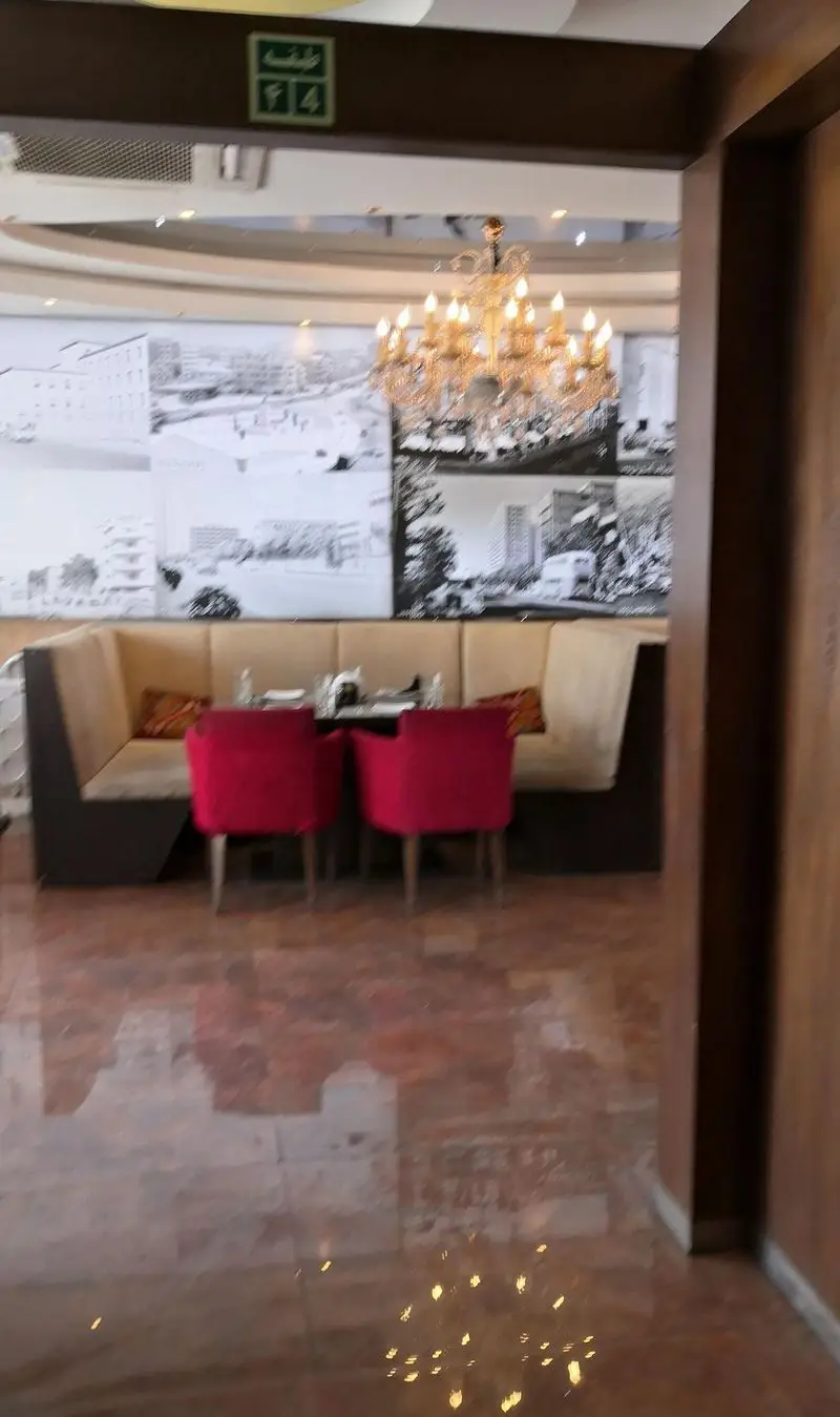نمایی جذاب از فضای داخلی رستوران تهران پاریس: مبلمان راحت، صندلی‌های قرمز شیک، لوستر بزرگ، و دکوراسیون مدرن با تصاویر شهر.