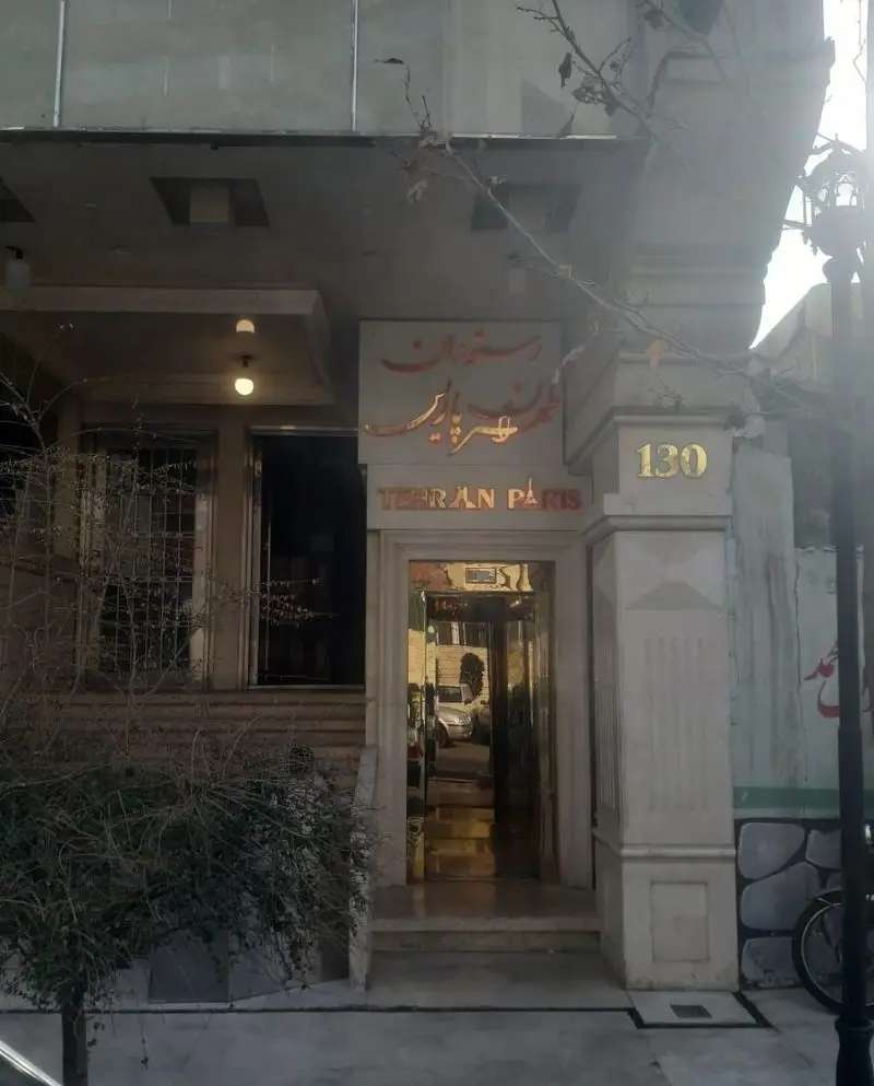 نمای بیرونی رستوران تهران پاریس در تهران، با تابلوی خوانا، شماره 130 و ورودی طلایی رنگ منعکس‌کننده خیابان.