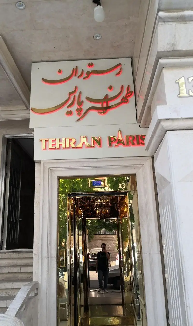 نمای بیرونی رستوران تهران پاریس با تابلوی شیک طلایی و نورپردازی قرمز، ورودی آسانسور براق و لوکس در خیابان ۱۳ تهران