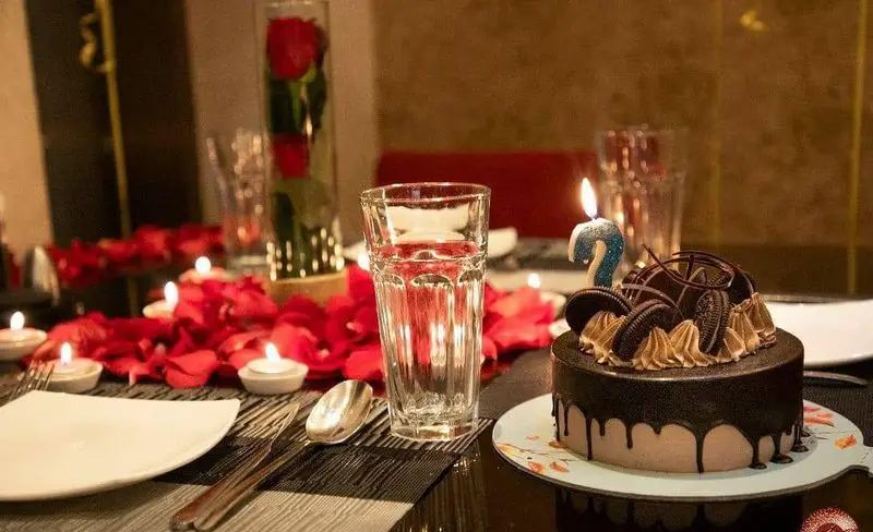 میز شام رمانتیک رستوران تهران پاریس با کیک شکلاتی و شمع، گلبرگ رز قرمز، ایده‌آل برای جشن تولد و سالگرد شما.