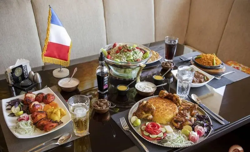 میز پر از غذاهای ایرانی و بین‌المللی با کباب، پلو زعفرانی، سالاد و نوشیدنی در رستوران تهران پاریس همراه با پرچم فرانسه.