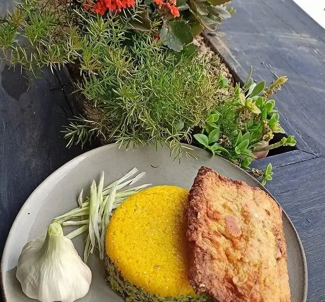 یک پرس غذای خوشمزه سبزی پلو با ماهی طلایی در رستوران 10forever، به همراه سیر تازه و سبزیجات. تجربه‌ای لذیذ از غذای ایرانی.