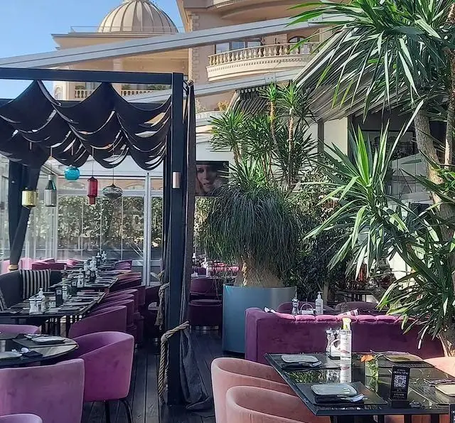فضای باز و دکوراسیون شیک رستوران 10forever با مبلمان بنفش مخملی، میزهای تیره، گلدان‌های بزرگ و سقف سایبان‌دار.