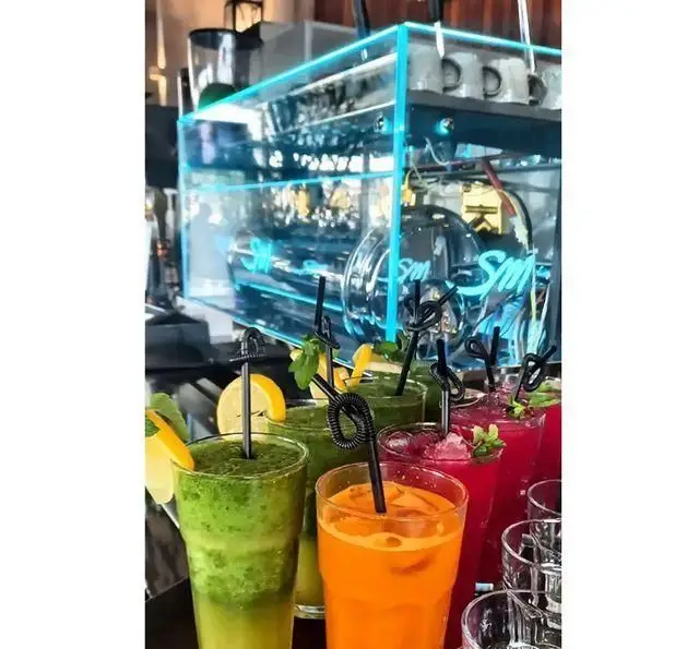نوشیدنی‌های تازه و رنگارنگ رستوران 10forever: اسموتی و آبمیوه‌های طبیعی سبز، نارنجی و قرمز در محیط مدرن با نور آبی شیک.