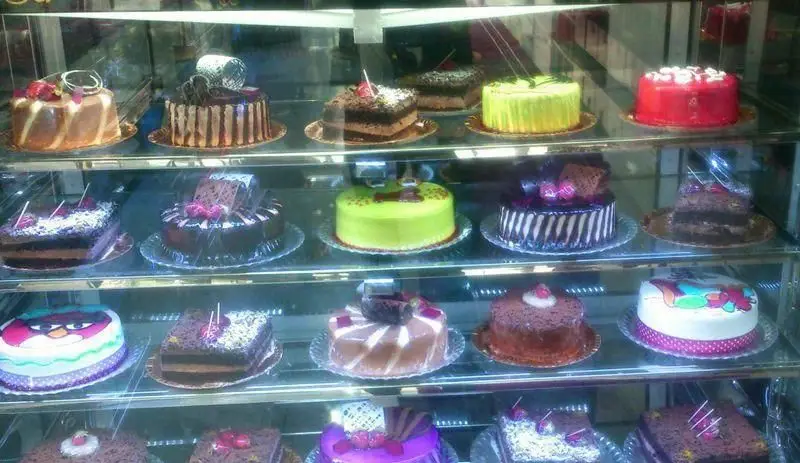 ویترین پر زرق و برق شیرینی سرای آنتیک شامل انواع کیک‌های تازه‌ و خوشمزه شکلاتی، میوه‌ای و دسرهای خاص و جذاب برای مشتریان.