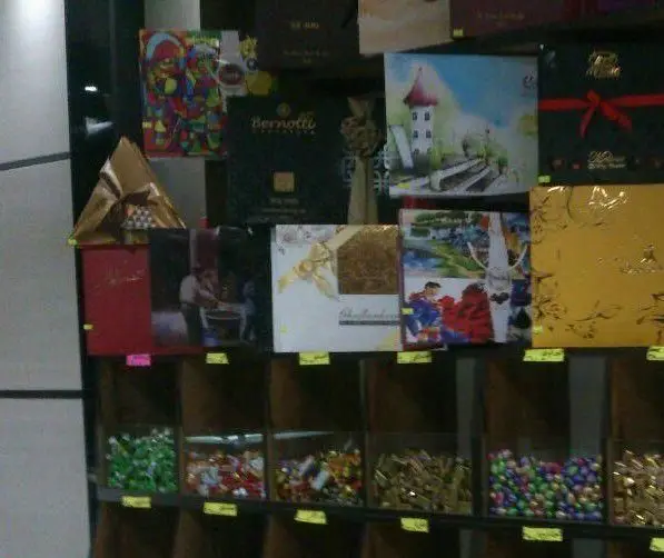 مجموعه‌ای متنوع از شیرینی‌های کادویی لوکس و شکلات‌های جعبه‌ای و فله، چیده شده در قفسه‌های شیرینی سرای آنتیک برای خرید آسان.