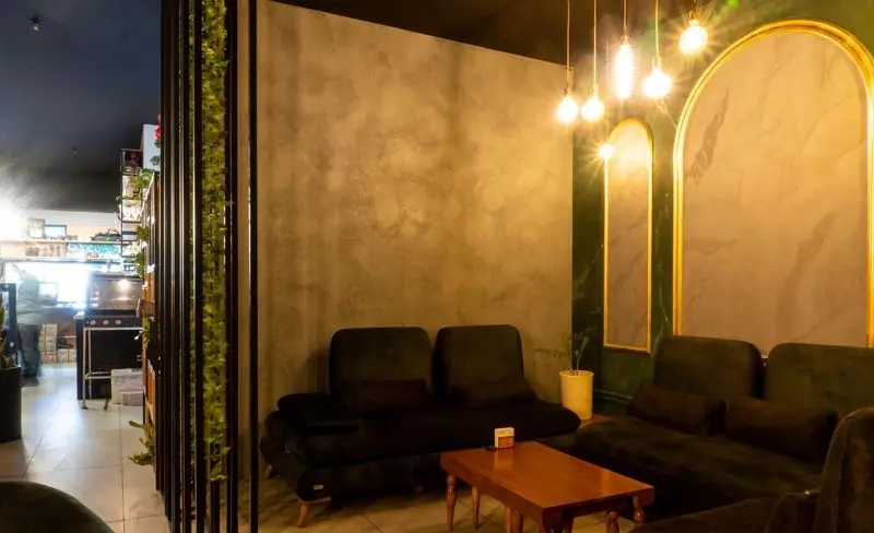 فضای داخلی کافه هاب، شیک و دنج با مبلمان تیره، دیوار بتنی و سبز زمردی با طاق های طلایی و نور گرم، محیطی عالی برای قهوه و آرامش.