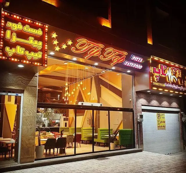 تصویر شب از نمای بیرونی فست فود و پیتزا تیپ تاپ با تابلوهای نئونی درخشان و طراحی داخلی شیک و مدرن، آماده پذیرایی از مشتریان.