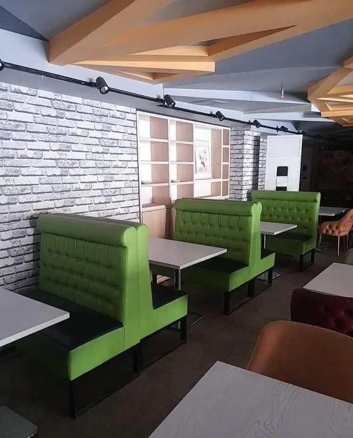محیط داخلی فست فود تیپ تاپ با دکوراسیون شیک و مدرن، شامل مبلمان سبز راحتی، میزهای سفید، دیوار آجری و نورپردازی خاص.