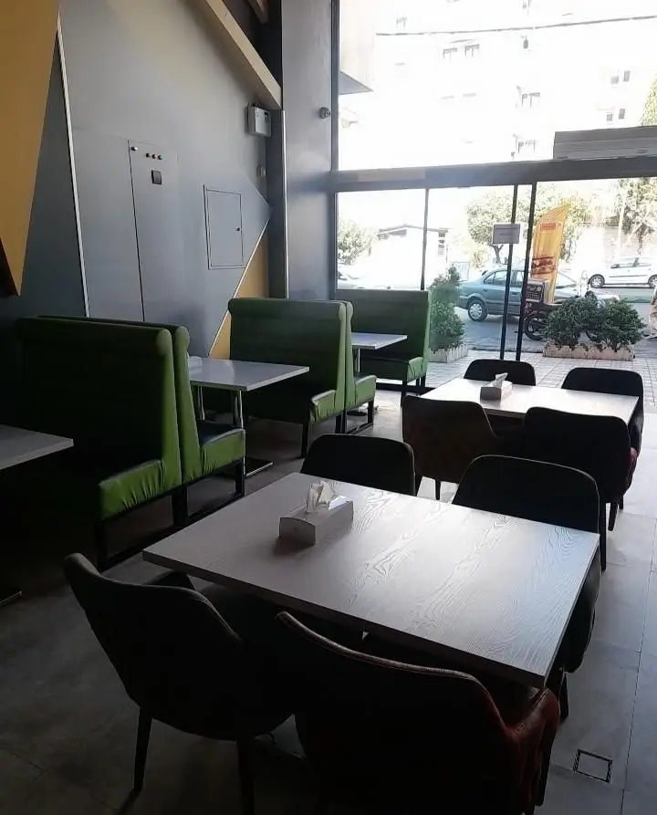 نمایی از فضای داخلی فست فود تیپ تاپ، شامل صندلی‌های سبز بوث و میزهای سفید چوبی در محیطی روشن و مدرن برای مشتریان.