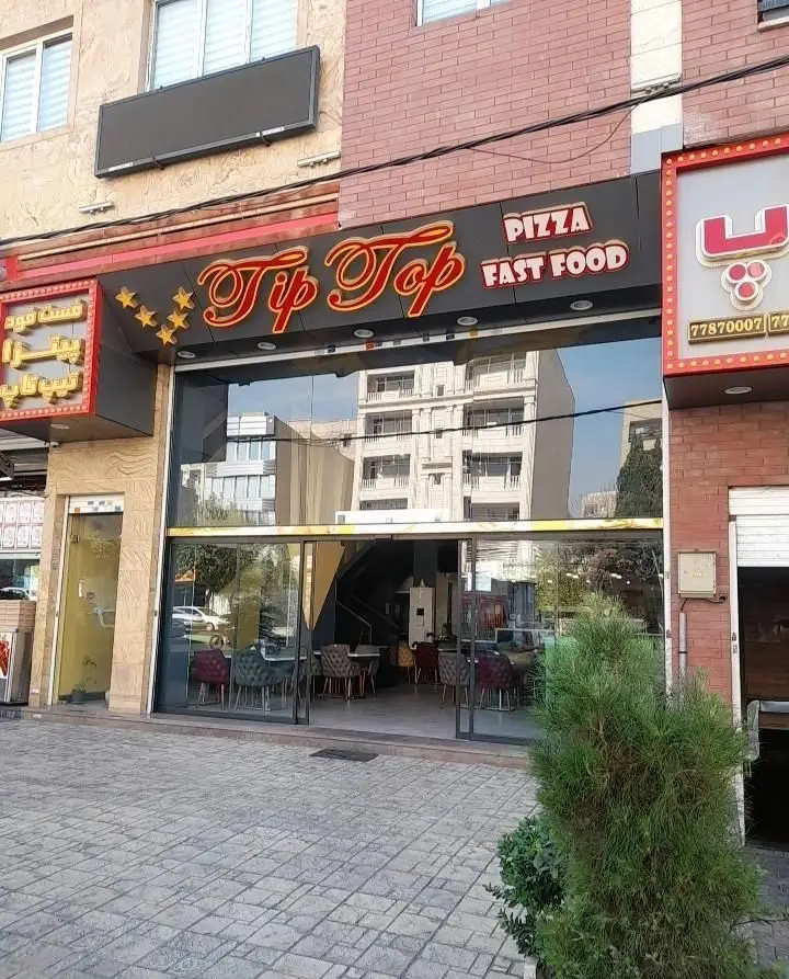 نمای بیرونی فست فود و پیتزا تیپ تاپ، با تابلوی بزرگ و جذاب 'Tip Top Pizza Fast Food' و ویترین شیشه‌ای در محیط شهری.