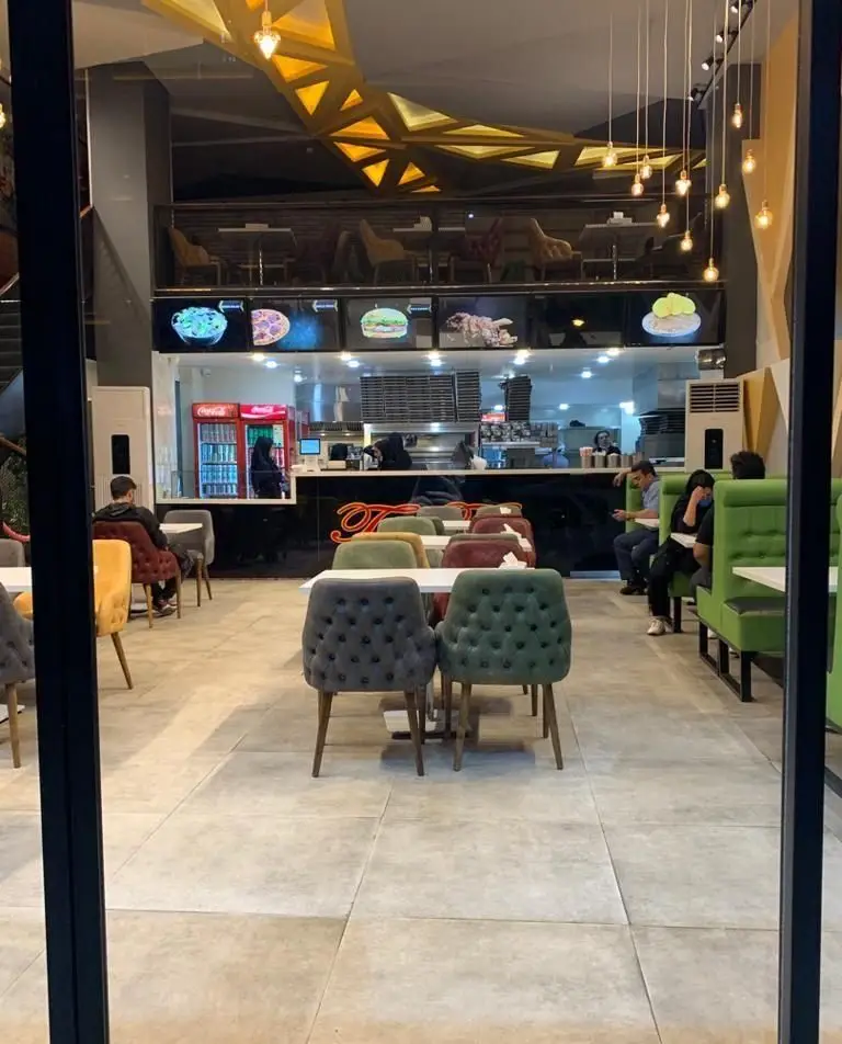 فضای داخلی مدرن فست فود تیپ تاپ، شامل میز و صندلی راحت، منوی دیجیتال غذاها و پیشخوان آماده سازی سفارشات با حضور مشتریان.