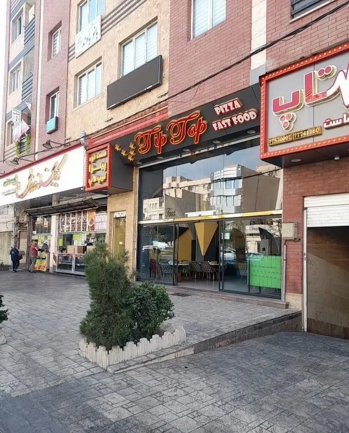 نمای خارجی و تابلوی درخشان فست فود تیپ تاپ (Pizza Fast Food) در یک روز آفتابی، مکانی مناسب برای سرو انواع پیتزا و غذاهای فوری در قلب شهر.