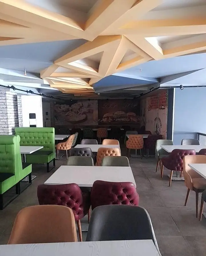 دکوراسیون داخلی مدرن و جذاب فست فود تیپ تاپ با سقف هندسی، میزهای سفید و صندلی‌های راحتی رنگارنگ.