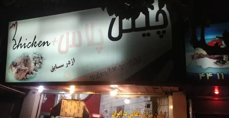 تابلوی روشن فست فود Chicken Plus، اولین ارائه‌دهنده مرغ ذغالی در ایران، با تصویر appetizing مرغ بریان و متن فارسی و انگلیسی.