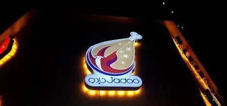 تابلوی درخشان فست فود جادو در تاریکی شب، با لوگوی جذاب مرغ سوخاری و نام تجاری جادو.