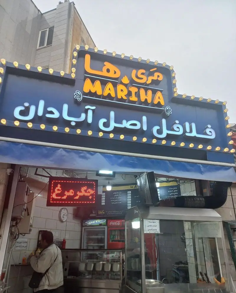 تصویر نمای بیرونی فست فود مری ها، رستوران تخصصی فلافل اصل آبادان، با تابلوی روشن و مشتری داخل مغازه.
