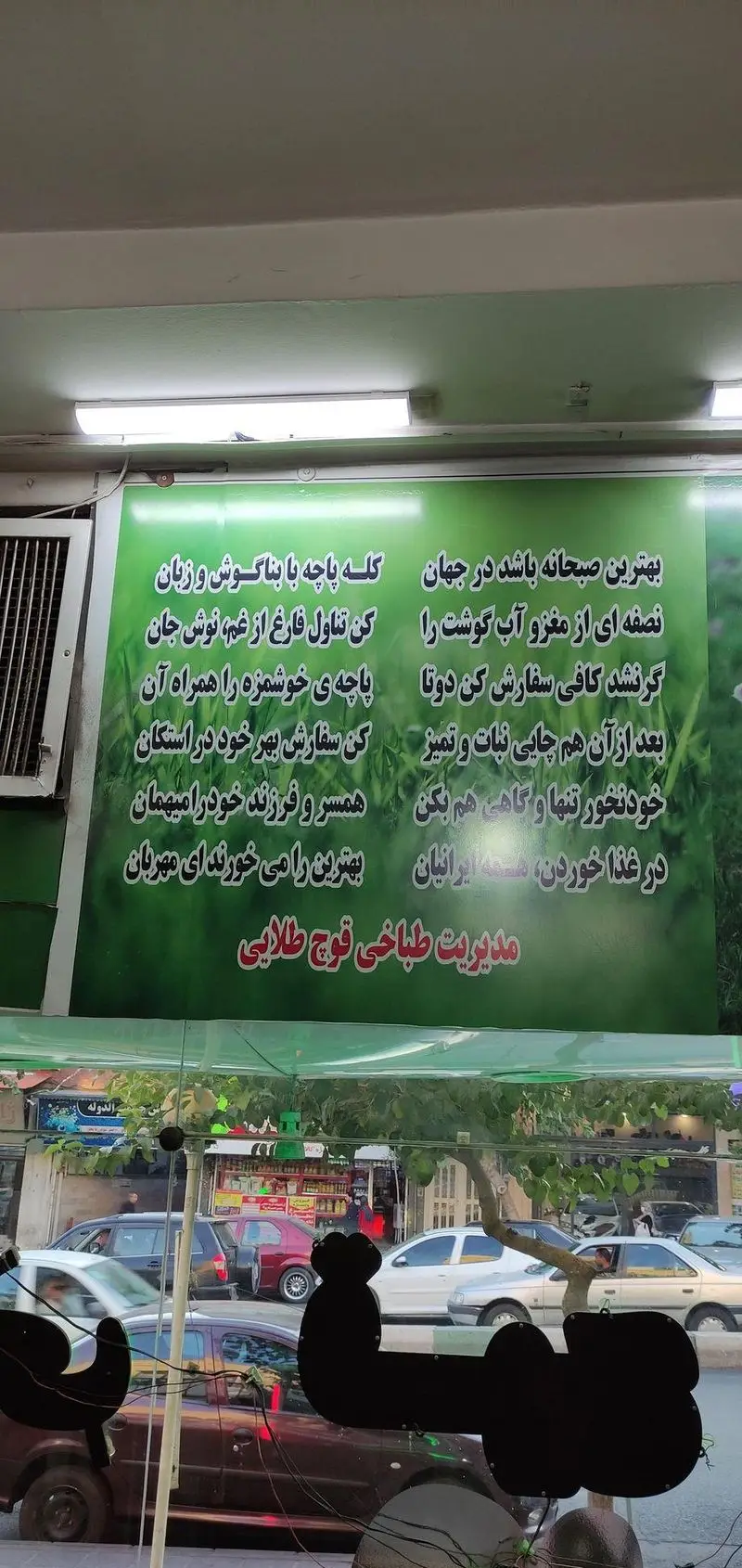 بنر تبلیغاتی طباخی قوچ طلایی شامل شعری درباره کله پاچه، غذای سنتی ایرانی و بهترین صبحانه، در ویترین فروشگاه.