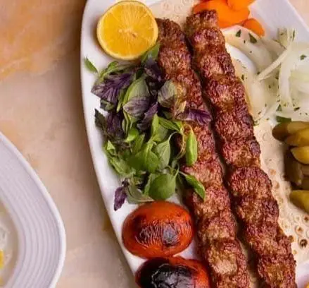 تصویری از کباب کوبیده لذیذ کافه رستوران بلوط همراه با سبزیجات معطر، گوجه کبابی و پیاز برای یک تجربه غذایی بی‌نظیر.