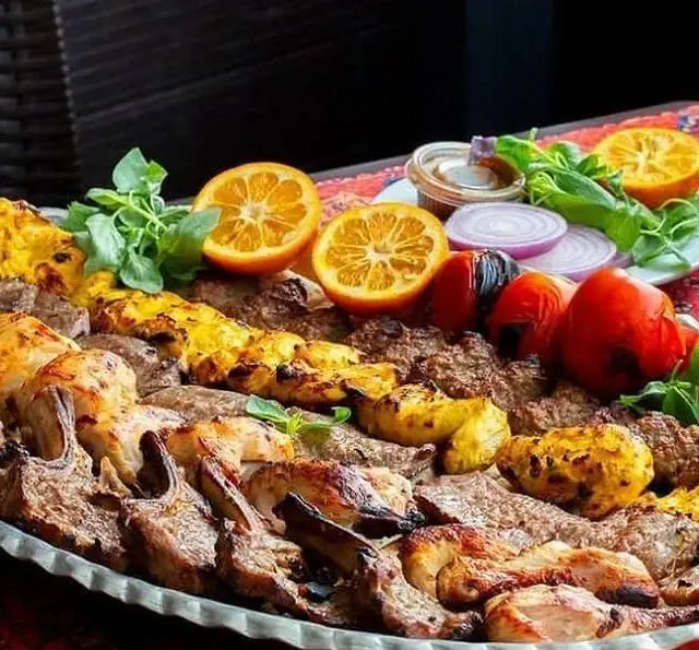 انواع کباب ایرانی شامل جوجه، شیشلیک و کوبیده در سینی بزرگ، همراه با دورچین پرتقال و گوجه در کافه رستوران بلوط.