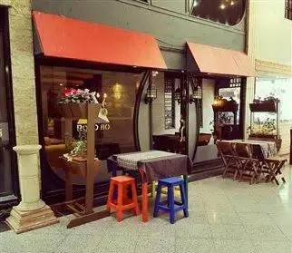 نمای بیرونی کافه جاده هشتاد با سایبان‌های قرمز، میز و صندلی‌های رنگارنگ در فضای باز، محیطی دنج و دلنشین برای میزبانی از مهمانان.