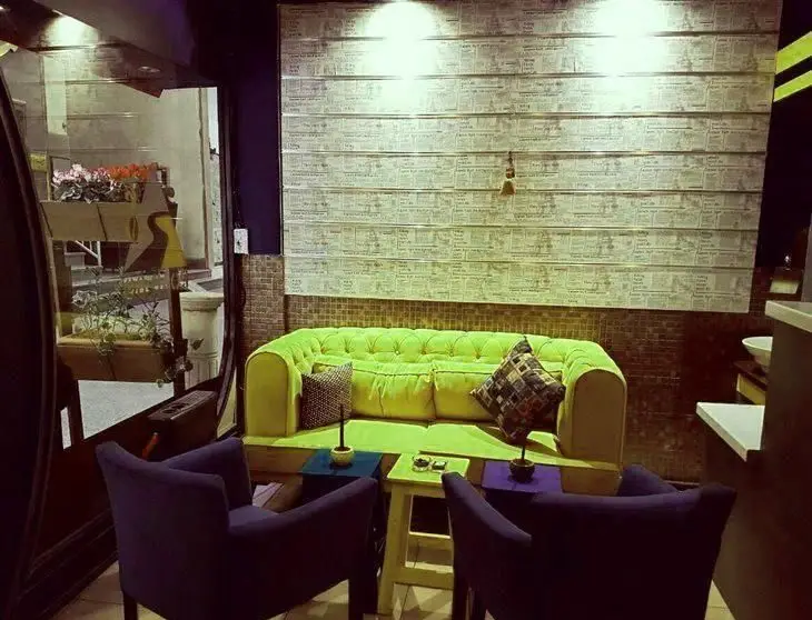 کافه جاده هشتاد: فضای داخلی دنج با مبل سبز روشن، صندلی‌های تک نفره بنفش و پنجره مشرف به فضای سبز بیرون