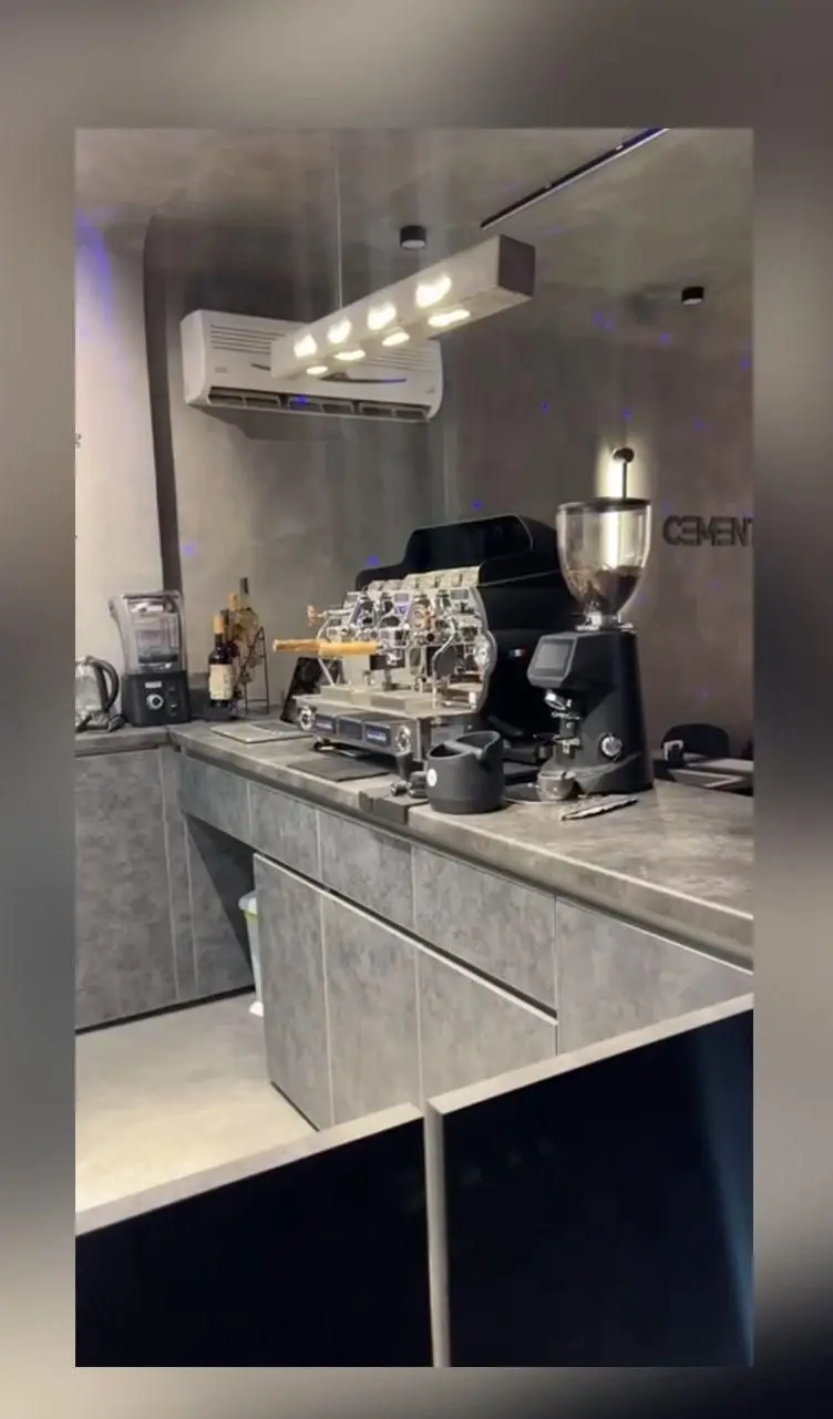 دکوراسیون شیک کافه سِمِنت با طراحی صنعتی و تجهیزات مدرن قهوه شامل دستگاه اسپرسوساز حرفه‌ای، آسیاب و لوازم کامل بار برای مشتریان