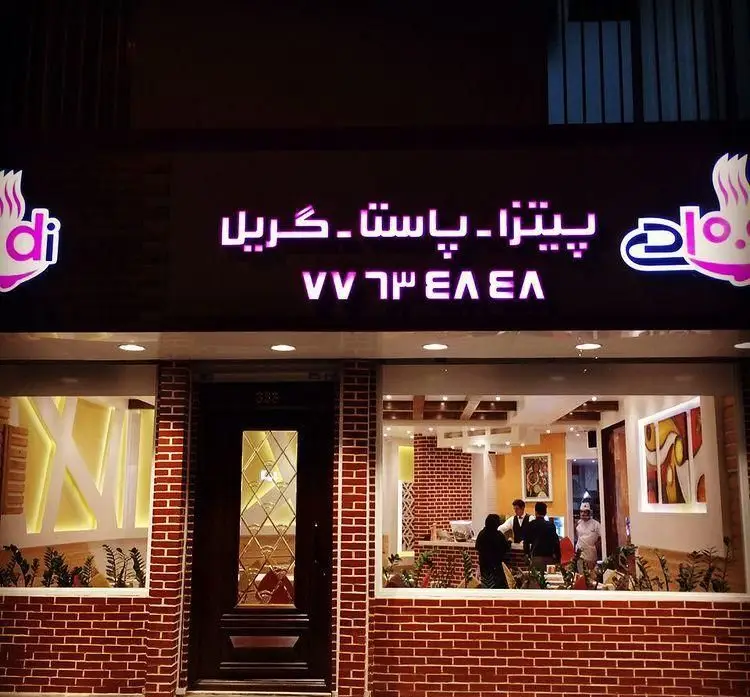 نمای خارجی شبانه رستوران ایتالیایی شادی با تابلوی نئون درخشان "پیتزا، پاستا، گریل" و نمای آجری گرم و دلنشین.