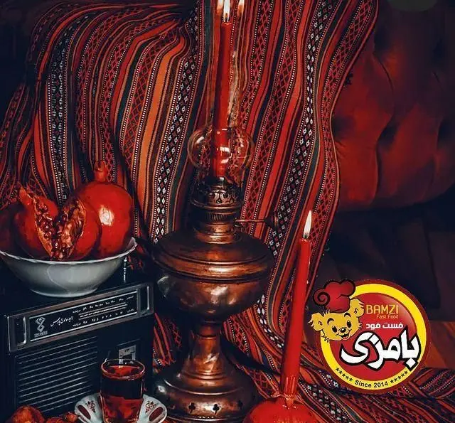 تصویری دلنشین از دورهمی شب یلدا با انار، چای و وسایل سنتی، نشان‌دهنده محیط گرم و صمیمی فست فود بامزی ازگل.